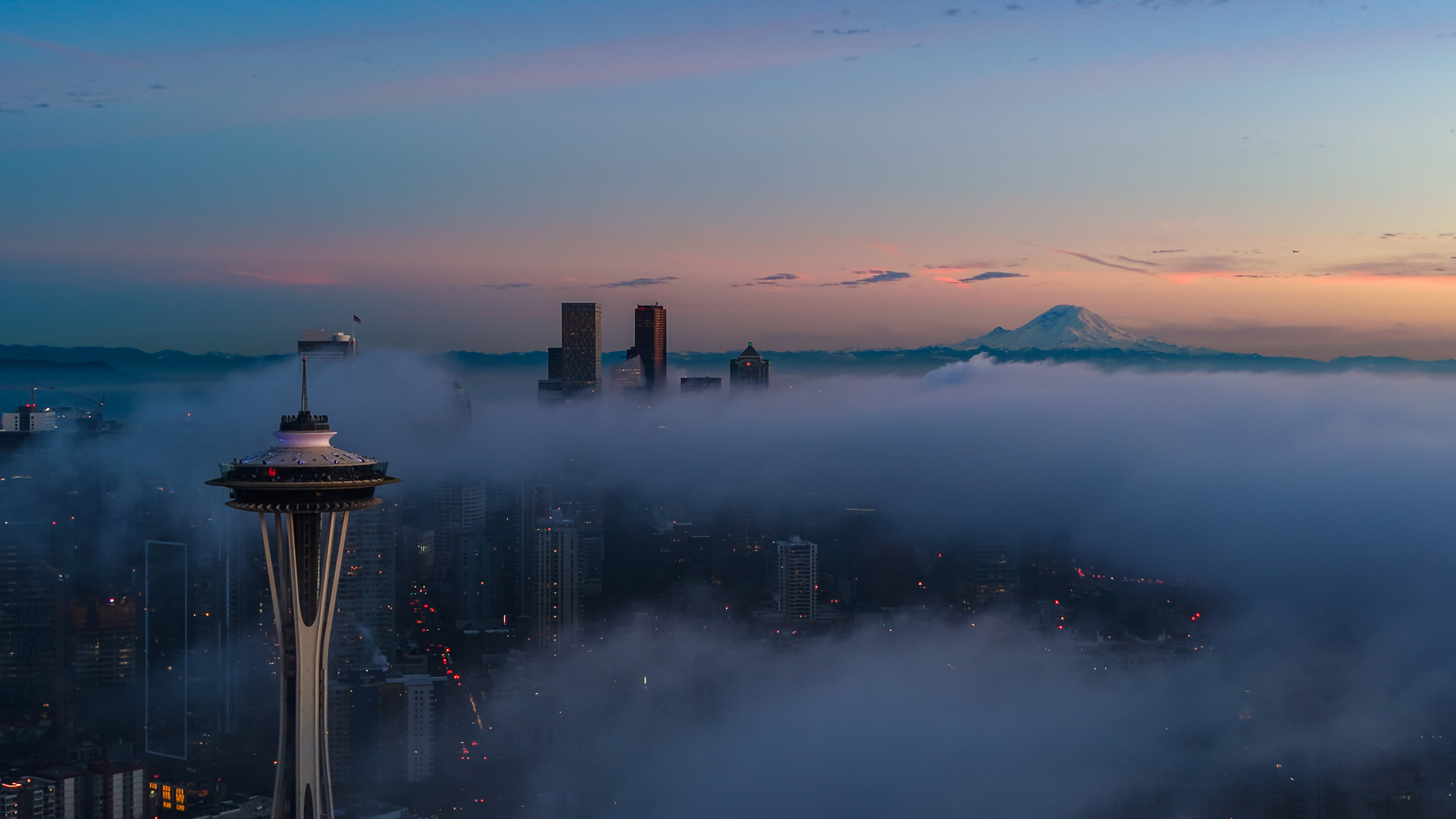 The Space Needle on the left and downtown towers and Mount Rainier on the right, a fog bank covering the city at dawn.