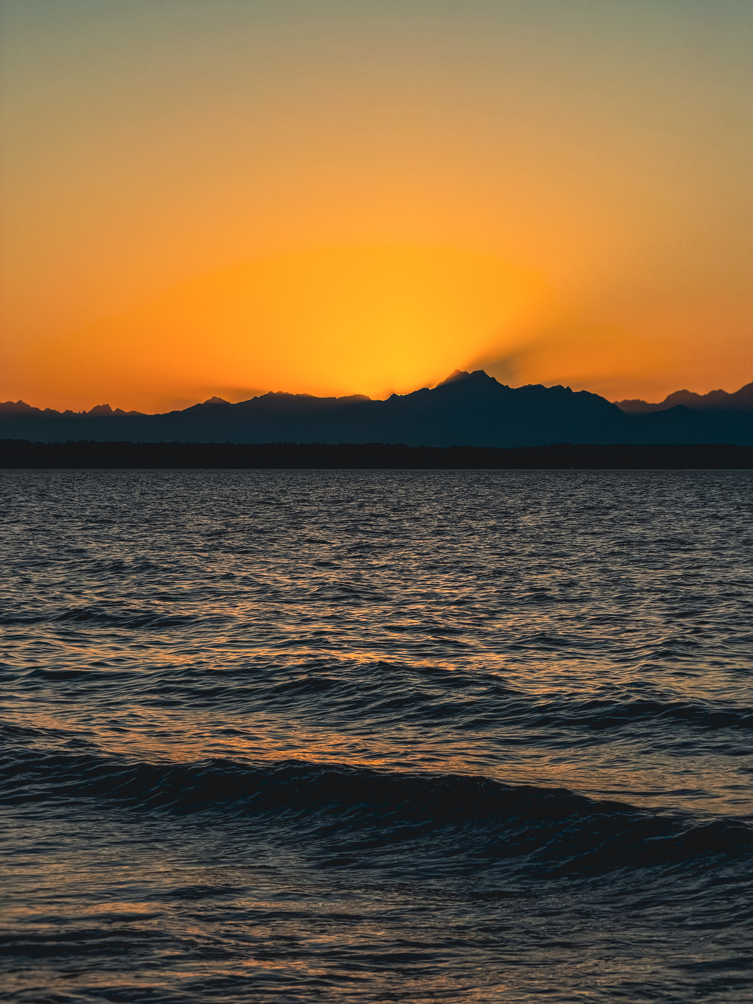 An orange sky over a mountain silhouette and dark rippled water.