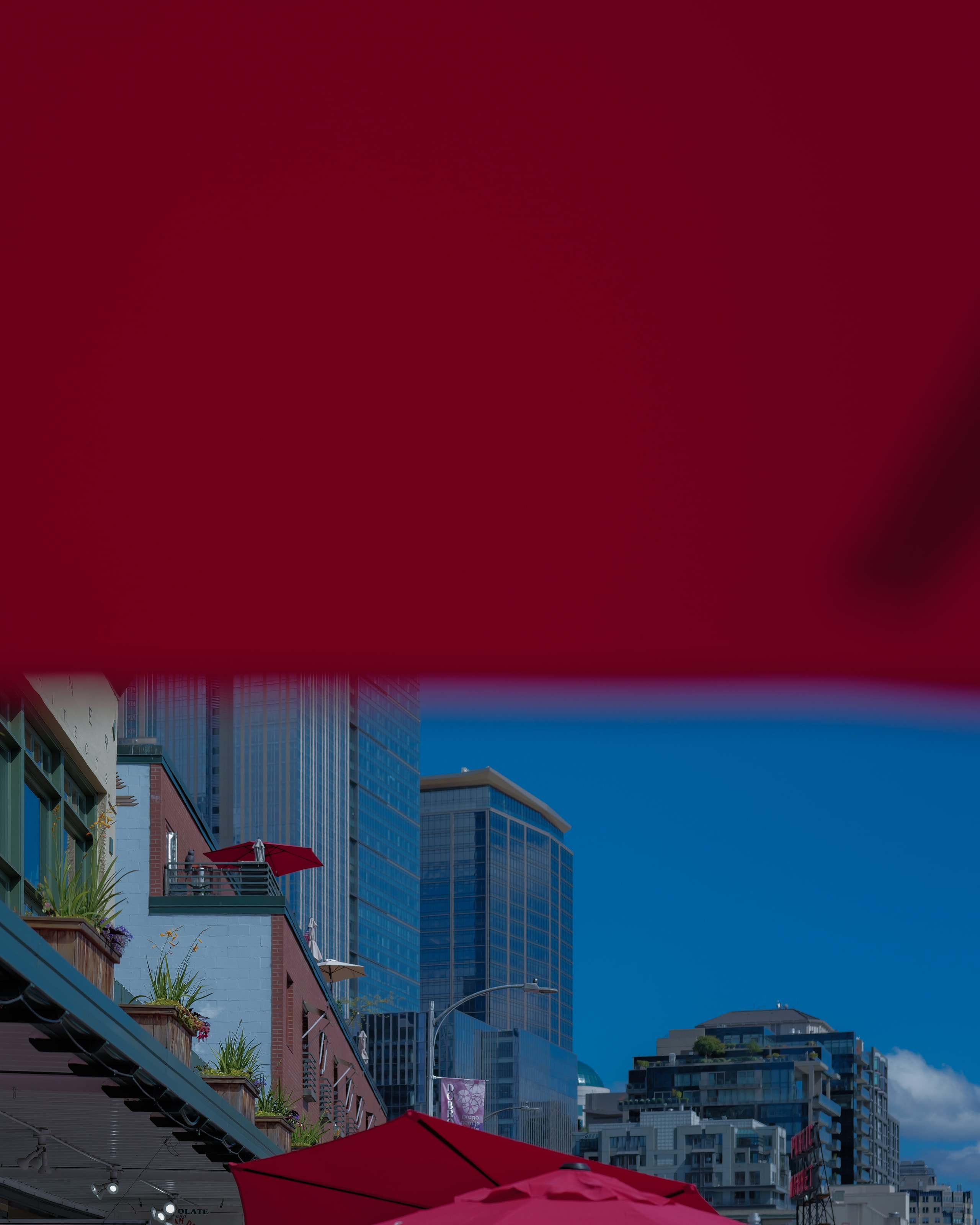 A red canopy filling the upper frame, with glass towers and blue sky beneath it.