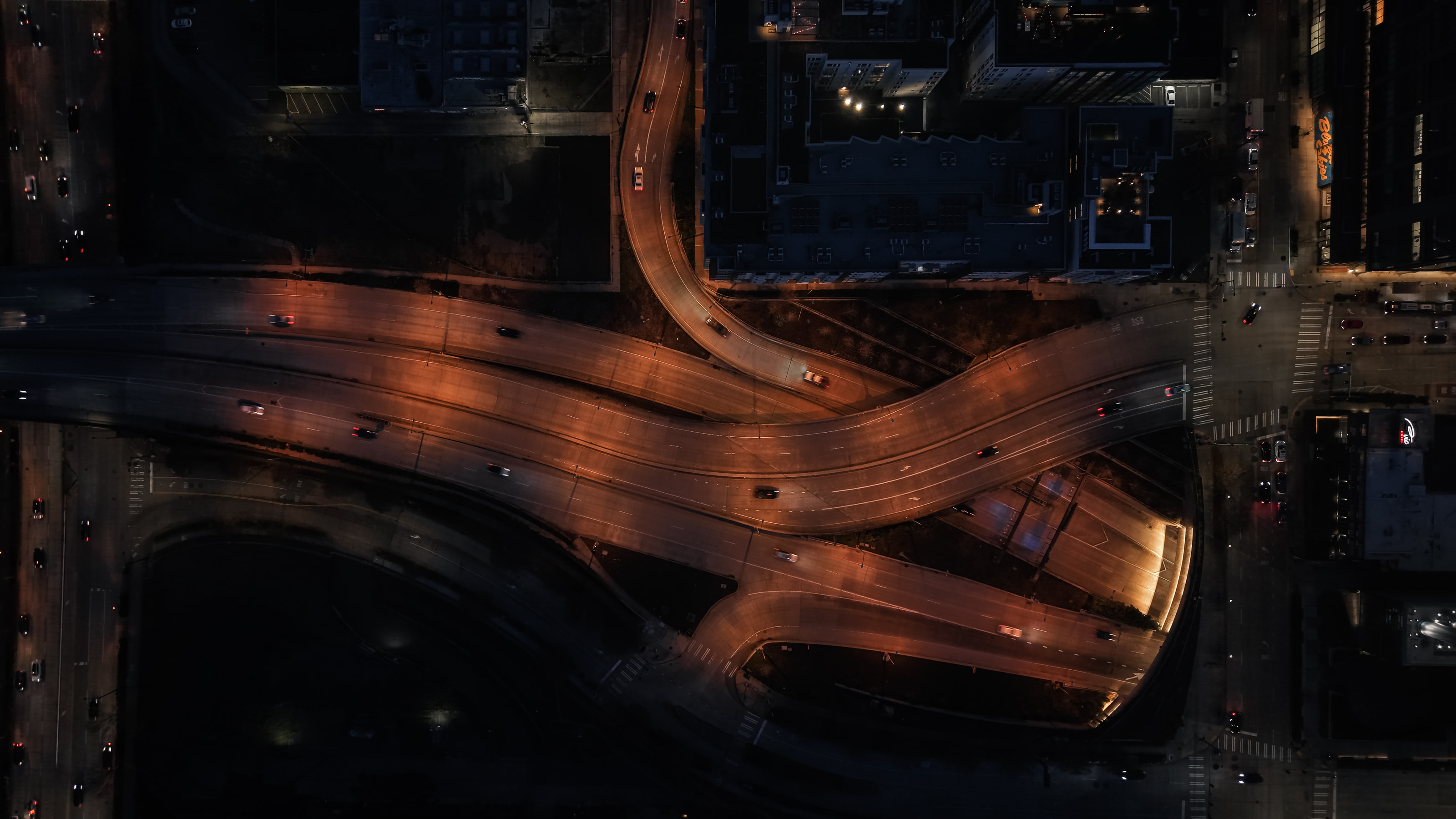 Straight-down aerial view of a freeway interchange at night, orange light on black.