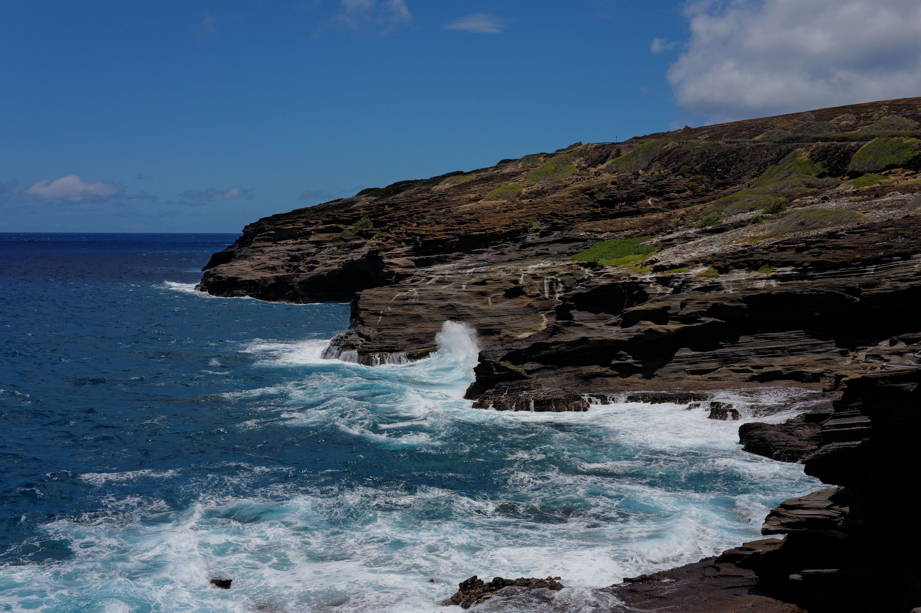 Layered lava cliffs with turquoise surf under cumulus clouds.