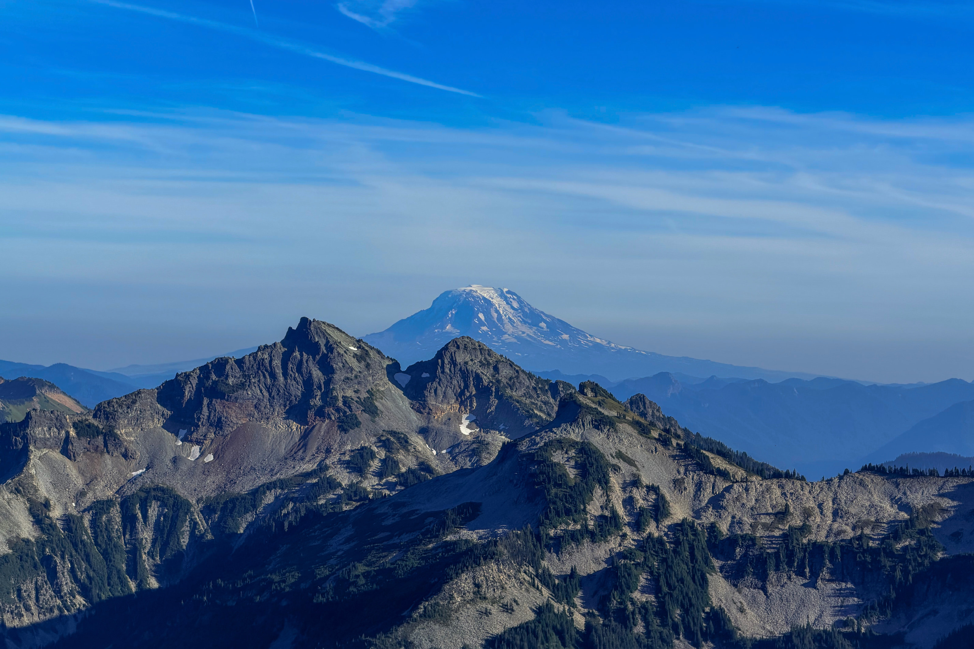 A distant snow-capped volcano above blue ridgelines in haze.